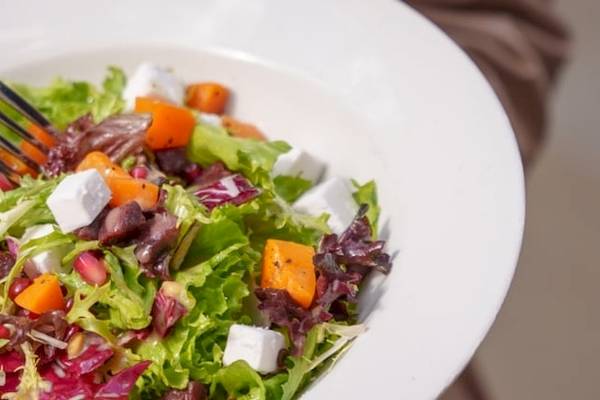 Ein Teller mit buntem Gemüsesalat, auf dem ein Löffel liegt.