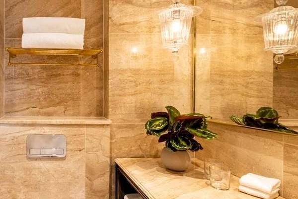 Das Badezimmer im Saint Hotel, London, mit goldenen Armaturen, marmorner Wandverkleidung und einem Regal mit Handtüchern.
