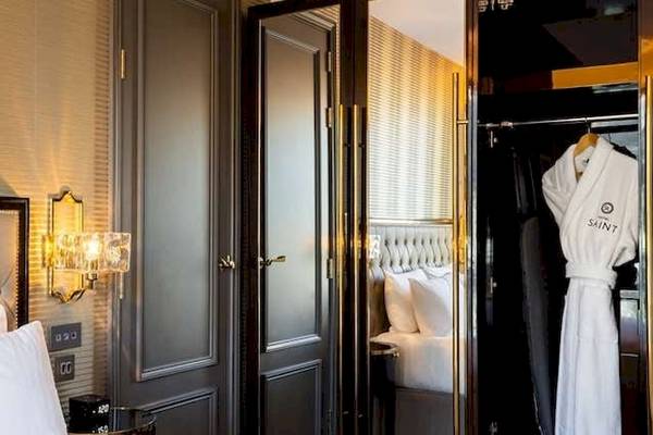 Ein elegantes Schlafzimmer im Saint Hotel, London, mit einem gepolsterten Bett, weißen Kissen und einem offenen Kleiderschrank mit einem weißen Bademantel.
