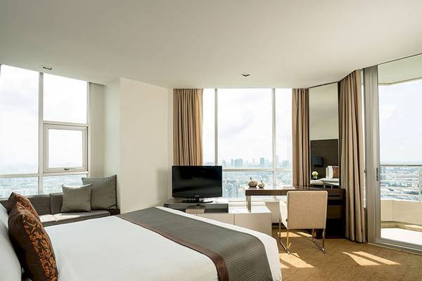 Ein modernes Hotelzimmer im JC Kevin Sathorn Bangkok mit großem Bett, Fernseher, Schreibtisch und Stadtaussicht.