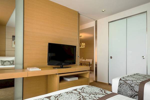 Hotelzimmer im JC Kevin Sathorn Bangkok mit Fernseher, Schreibtisch und zwei Betten.