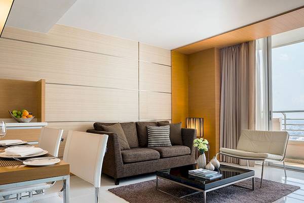 Wohnzimmer im JC Kevin Sathorn Bangkok Hotel mit moderner Einrichtung, einem Sofa, Tisch und Blick auf die Stadt.