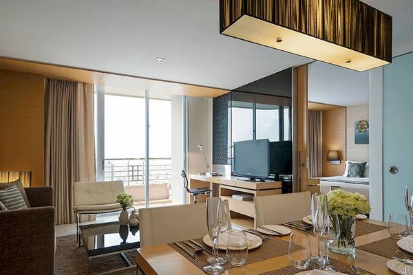 Inneneinrichtung des JC Kevin Sathorn Bangkok Hotels mit Esstisch, Fernseher und Blick auf die Stadt.
