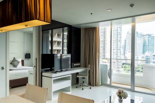 Innenansicht eines Zimmers im JC Kevin Sathorn Bangkok Hotel mit Schreibtisch, Fernseher und Balkon.