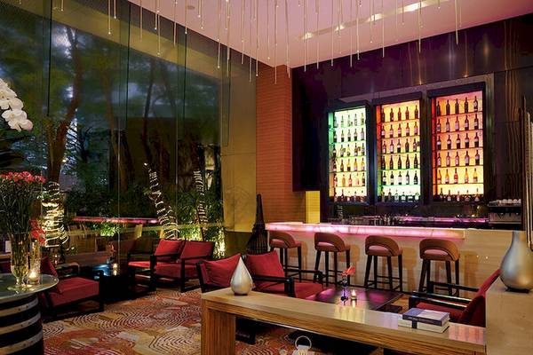 Loungebereich im JC Kevin Sathorn Bangkok Hotel mit roten Stühlen, Bar und beleuchteten Flaschen.