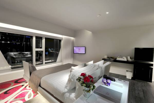Ein elegantes Schlafzimmer im Mode Sathorn Hotel mit großem Bett, Blumenvase und Fernseher an der Wand.
