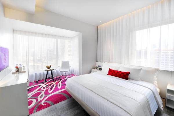 Schlafzimmer im Mode Sathorn Hotel mit großem Bett, weißen Wänden und rosa Teppich.
