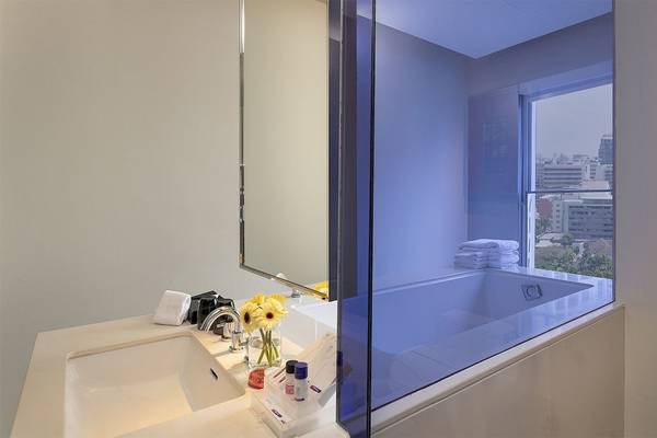 Badezimmer im Mode Sathorn Hotel mit Badewanne und Dusche, gelben Blumen im Glas und Blick auf die Stadt.