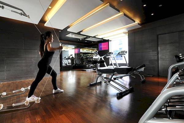 Eine Frau trainiert im Fitnessraum des Mode Sathorn Hotels, umgeben von verschiedenen Trainingsgeräten.