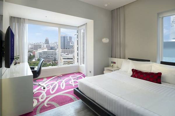 Schlafzimmer des Mode Sathorn Hotels mit Blick auf die Stadt aus großen Fenstern.