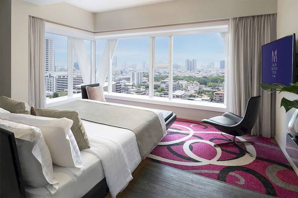Zimmer im Mode Sathorn Hotel mit einem großen Bett, Fenstern und Blick auf die Stadt.