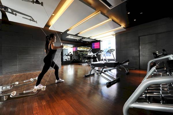 Fitnessraum im Mode Sathorn Hotel mit Frau, die an einem Zuggerät trainiert.