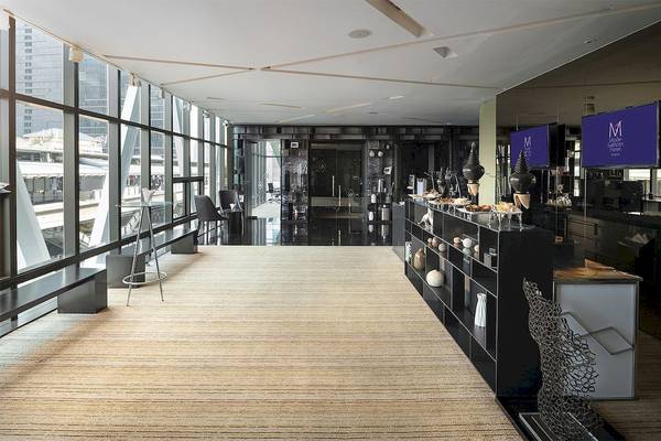 Innenansicht des Empfangsbereichs des Mode Sathorn Hotel mit großen Fenstern, moderner Einrichtung und Blick auf die Stadt.