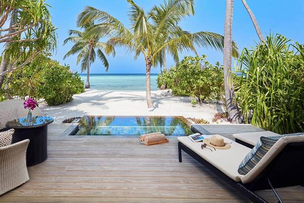 Außenbereich des Amari Havodda Maldives mit Pool, Strand und Palmen.