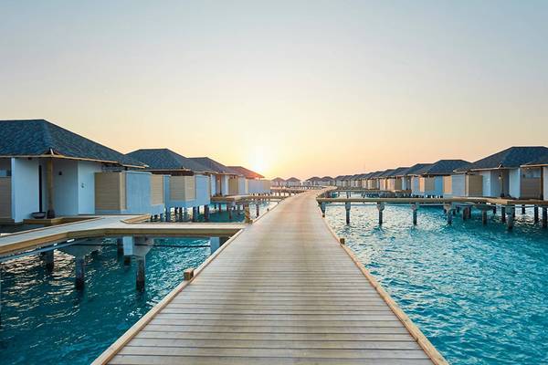 Sonnenuntergang am Amari Havodda Maldives mit Wasservillen auf Stegen im Wasser.