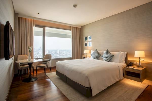 Innenansicht eines Zimmers im AVANI+ Riverside Bangkok Hotel mit großem Bett, Tisch und Blick auf die Stadt.