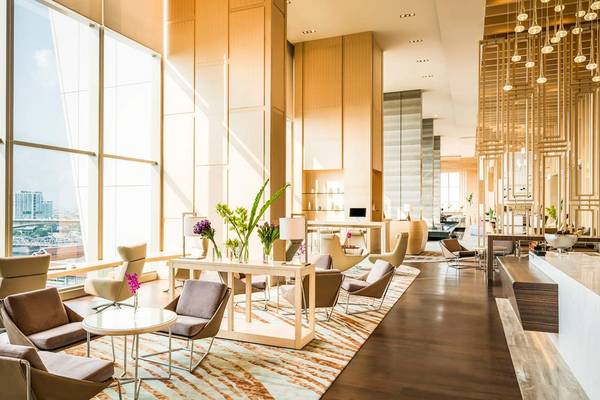 Lobby des AVANI+ Riverside Bangkok Hotels mit Möbeln, Pflanzen und Blick auf die Stadt.