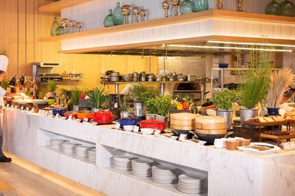 Restaurant im AVANI+ Riverside Bangkok mit Buffet und Köchen, die Speisen zubereiten.