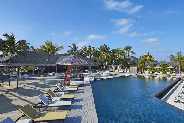 Außenpoolbereich des Amari Havodda Maldives Hotels mit vielen Liegestühlen und Palmen.