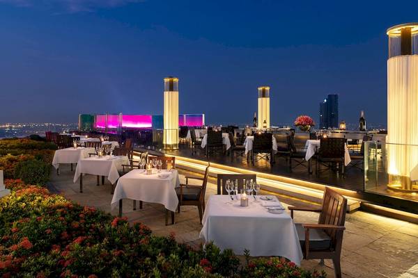 Dachterrasse des Tower Club At Lebua bei Nacht mit beleuchteten Säulen und Tischen.