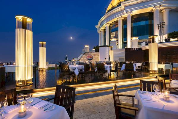 Außenbereich des Tower Club At Lebua Restaurants bei Nacht mit beleuchteten Säulen und Tischen.