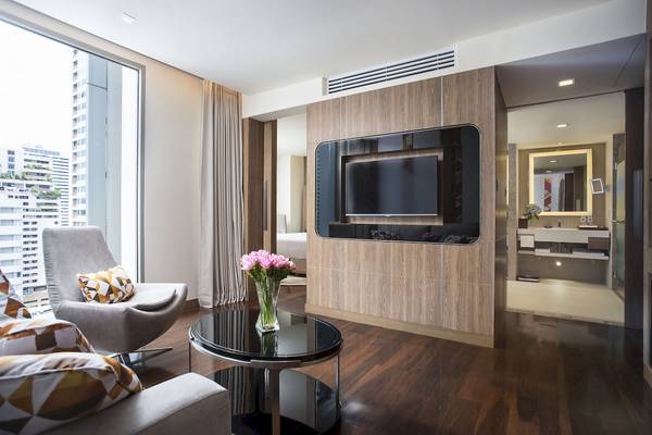 Wohnzimmer des Novotel Bangkok Sukhumvit 20 mit Fernseher, Tisch, Sessel und Blumenvase.