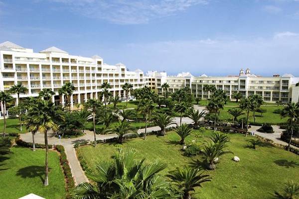 Außenansicht des Riu Gran Canaria Hotels mit vielen Palmen und grünen Rasenflächen.