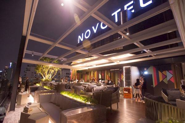Nachtansicht der Terrasse des Novotel Bangkok Sukhumvit 20 Hotels mit Beleuchtung und Gästen.