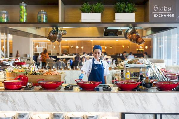 Buffet-Tisch im Novotel Bangkok Sukhumvit 20 mit einer lächelnden Mitarbeiterin, die rote Töpfe serviert.