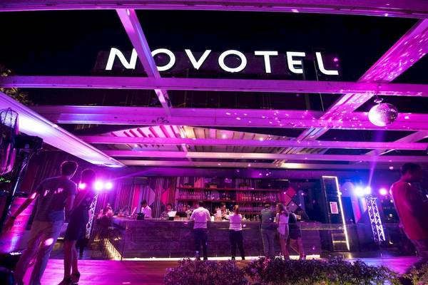 Die Bar des Novotel Bangkok Sukhumvit 20 bei Nacht mit violettem Licht und Gästen an der Bar.