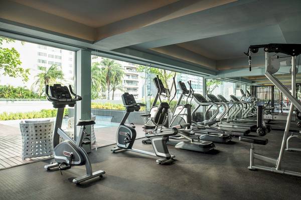 Innenansicht des Fitnesscenters im Novotel Bangkok Sukhumvit 20 mit mehreren Laufbändern und Blick auf das Schwimmbad