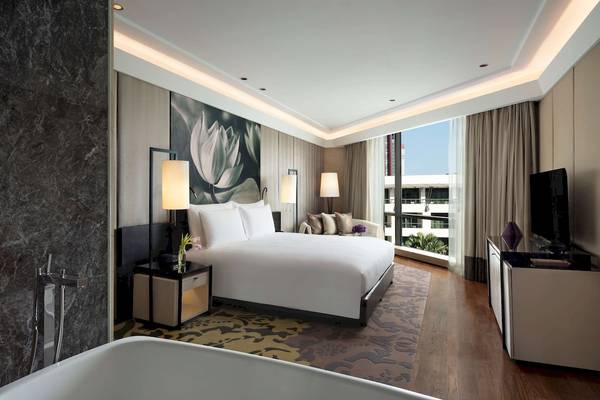 Schlafzimmer des Siam Kempinski Hotel Bangkok mit großem Bett, Marmorwand, Badewanne und Ausblick.