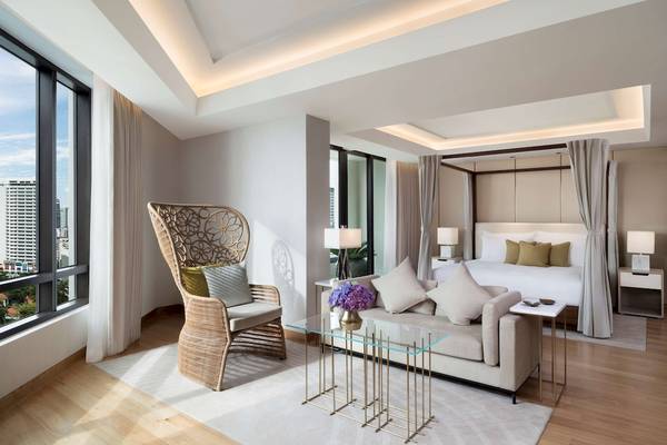 Innenansicht der Suite im Siam Kempinski Hotel Bangkok mit großem Bett, Wohnzimmer und Aussicht auf die Stadt.