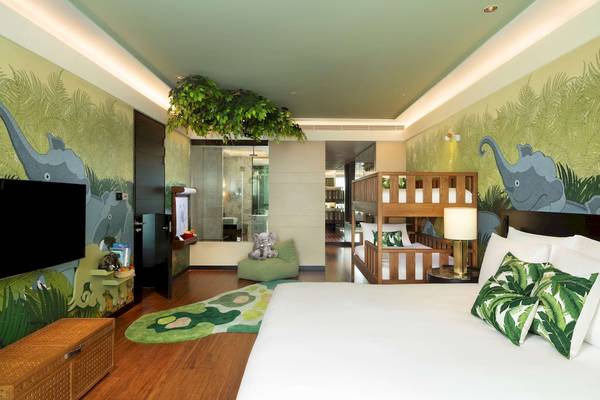 Kinderzimmer im Siam Kempinski Hotel Bangkok mit Elefantenmalerei an der Wand, Betten, grünen Kissen und einem Fernseher.