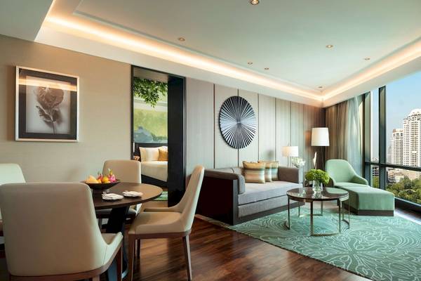 Wohnzimmer im Siam Kempinski Hotel Bangkok mit Sofa, Tisch, Esstisch und Fenstern.