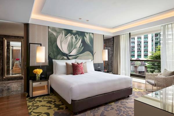Schlafzimmer im Siam Kempinski Hotel Bangkok mit großem Bett, Blumen, und Ausblick auf die Stadt.