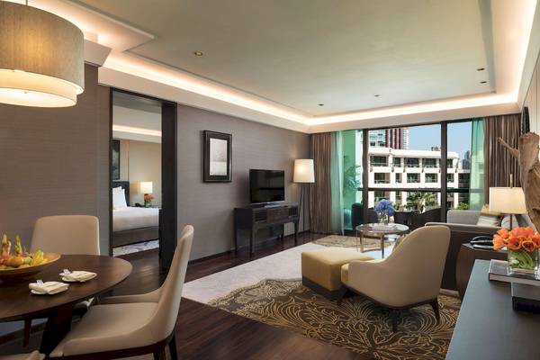 Innenansicht des Wohnzimmers im Siam Kempinski Hotel Bangkok mit Möbeln und Fernseher.