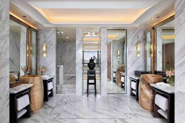 Innenansicht des Badezimmers im Siam Kempinski Hotel Bangkok mit Marmorwänden, runden Waschbecken und großen Spiegeln.