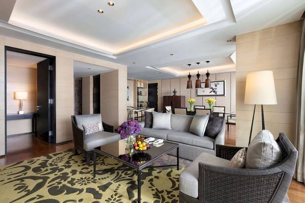 Wohnzimmer des Siam Kempinski Hotel Bangkok mit grauem Sofa, Tisch und Dekor.