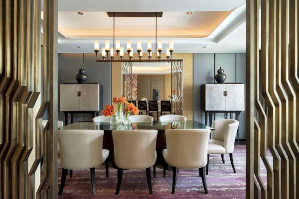 Esszimmer im Siam Kempinski Hotel Bangkok mit Glastisch, gepolsterten Stühlen und floraler Dekoration.
