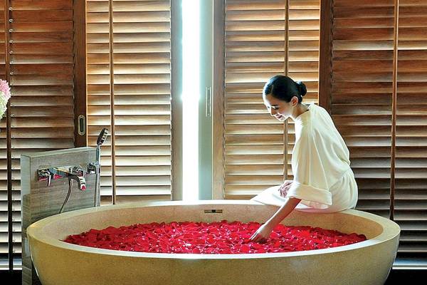 Eine Frau im Siam Kempinski Hotel Bangkok genießt ein Bad in einer Wanne voller roter Rosen.