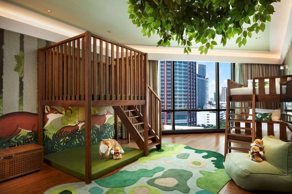 Kinderzimmer im Siam Kempinski Hotel Bangkok mit Holzbetten, grüner Spielwiese und Blick auf die Stadt.