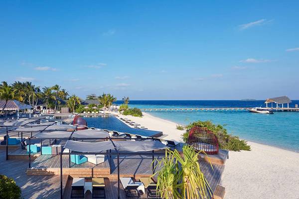Amari Havodda Maldives Strand mit mehreren Liegebereichen und einem Pier im Hintergrund.