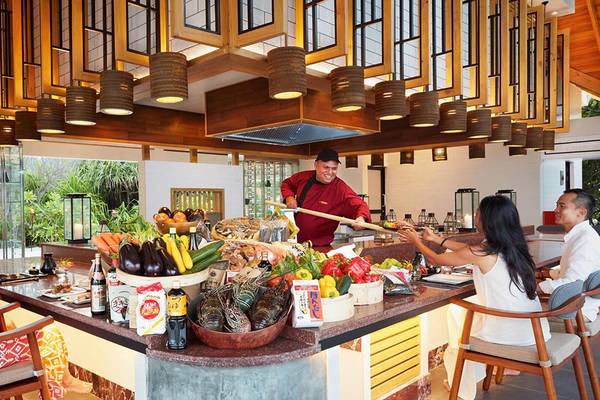 Menschen sitzen an einem Buffettisch im Amari Havodda Maldives Hotel und essen mit einem Koch.