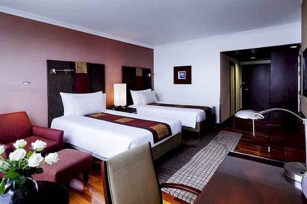 Doppelzimmer im Pullman Bangkok Hotel G mit zwei Betten, Schreibtisch, Stuhl, Couch und Blumenvase.