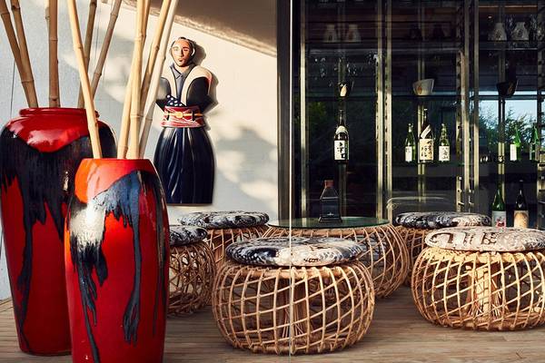Hotellobby des Amari Havodda Maldives mit roten Vasen, Bambusstangen, Sitzhockern und einer Glasvitrine.