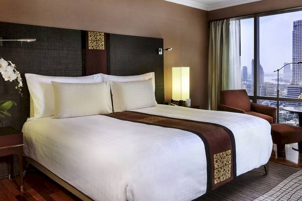 Schlafzimmer im Pullman Bangkok Hotel G mit Bett, Lampe und Blick auf die Stadt.