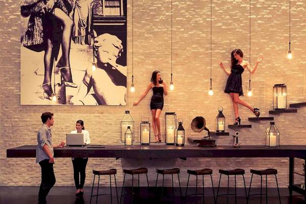 Innenbereich des Pullman Bangkok Hotel G mit Personen an einer Bar und einer Frau auf der Treppe.