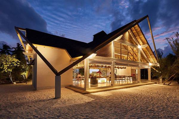 Außenansicht des Amari Havodda Maldives Hotel bei Nacht mit beleuchteter Fassade und Gästen im Restaurantbereich.