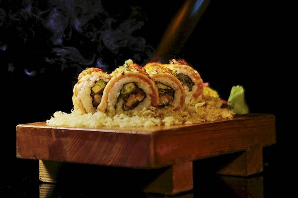 Sushi mit Raucheffekt auf einer Holzplatte serviert, mit Reis und Gemüse gefüllt